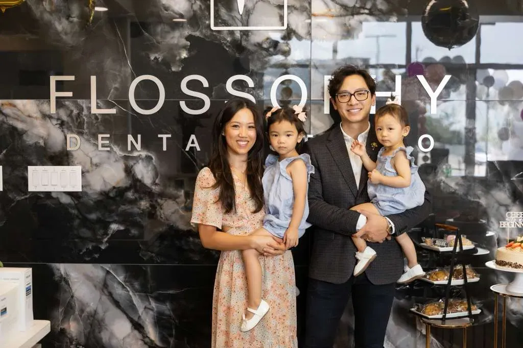 Dr. Matthew Le with his wife and two daughters in front of the marble Flossophy Dental Studio sign wall on opening day in Haltom City